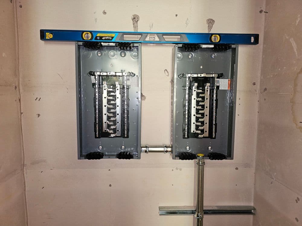 Dual electrical panels installed with a level on a drywall background.