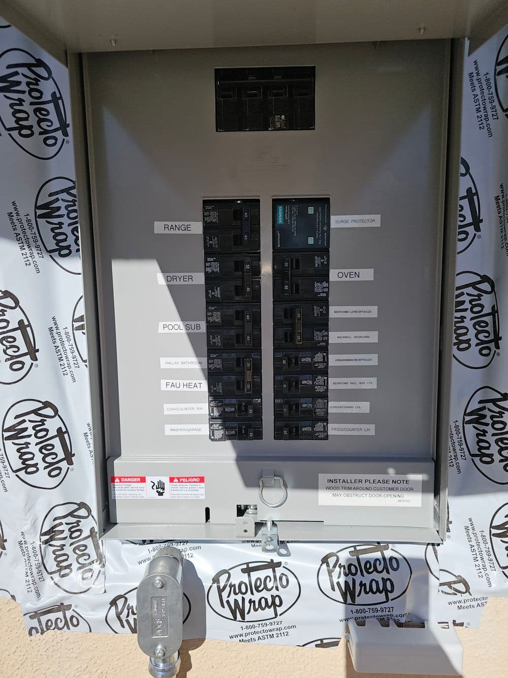 Electrical panel with labeled breakers and protective wrapping for safety and installation notes.