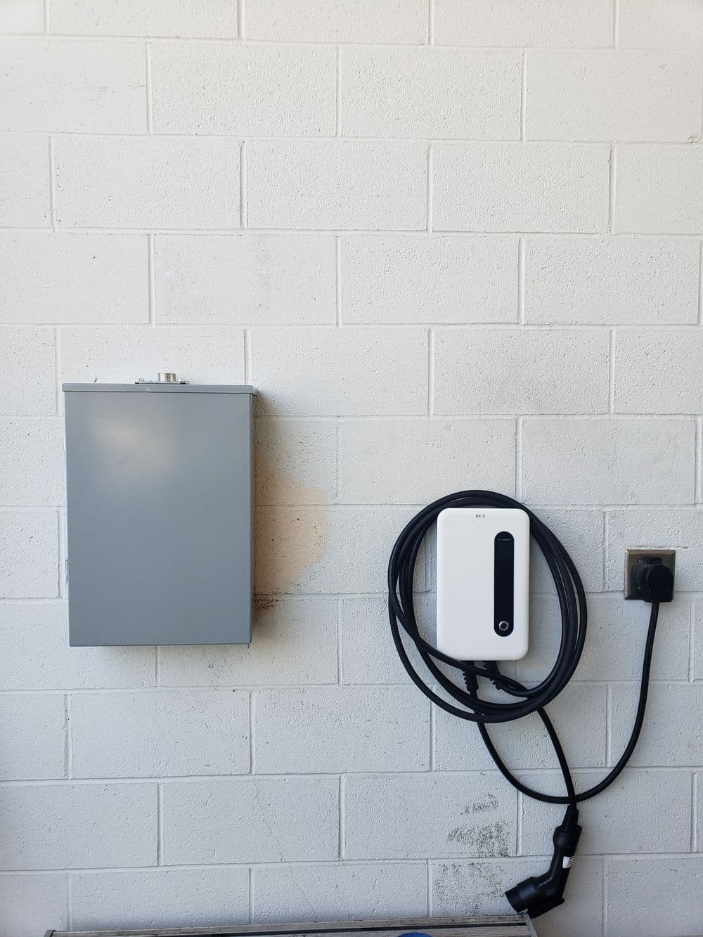 Electric vehicle charging station mounted on a wall with a gray electrical box nearby.