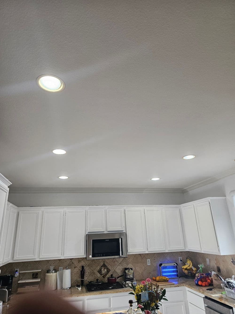 Bright modern kitchen with recessed lighting and white cabinets. Potted flowers on countertop.