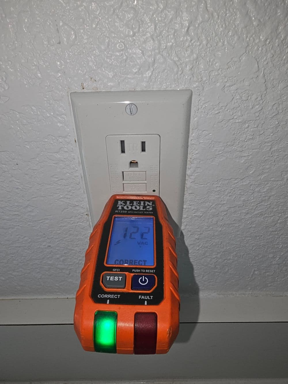 Klein Tools voltage tester measuring 112 VAC on wall outlet, with LED indicator lights.